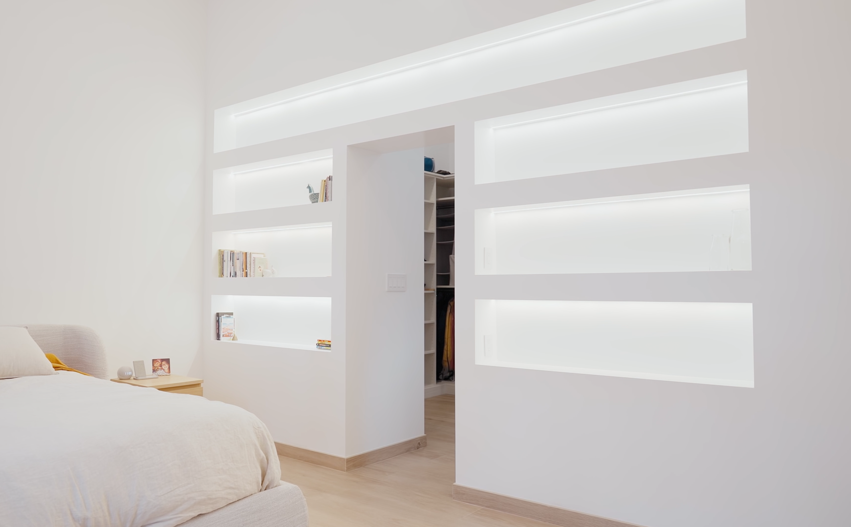 Bedroom with illuminated built-in shelving wall and hidden closet entry